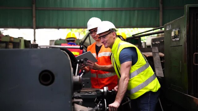 Mechanic holding a wrench and a tablet standing in front of an machine. Worker in manufacturing plant at Machine control panel. Milling machine operator working in factory workshop.