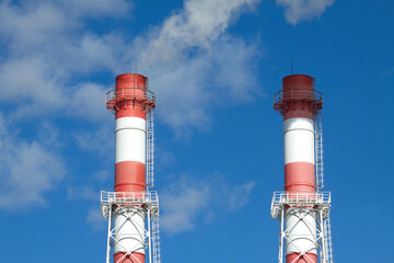 Top part of two big color industrial smoke pipes over blue sky with clouds front view