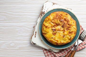 Homemade Spanish tortilla - omelette with potatoes on plate on white wooden rustic background top view. Traditional dish of Spain Tortilla de patatas for lunch or snack, overhead. Space for text
