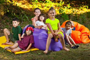Children rest in nature. Boys and girls play on an inflatable sofa. Summer vacation in the garden.