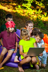 Children play in nature with a laptop. Boys and girls are resting in a tent camp. Children sit on a purple inflatable sofa in summer.