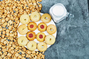 Scattered alphabet crackers, a plate of cookies and a jar of milk on marble background