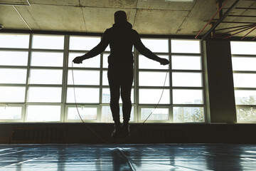 Fototapeta na wymiar Athlete man jumping rope in the training room in front of large panoramic windows