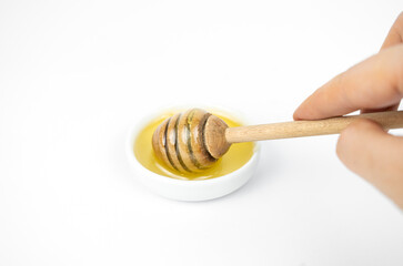 Liquid honey pouring with wooden stick in small white plate.