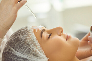 Smiling womans face getting skincare procedure of applying nourishing oil on skin - obrazy, fototapety, plakaty