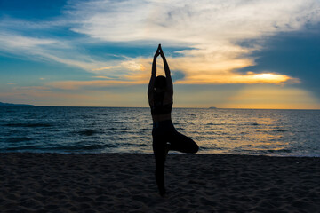 Silhouette image of a woman doing yoga on the beach at sunset. 
Young healthy woman, Asian girl practice Yoga on the beach Sunrise morning day Yoga on the beach healthy woman