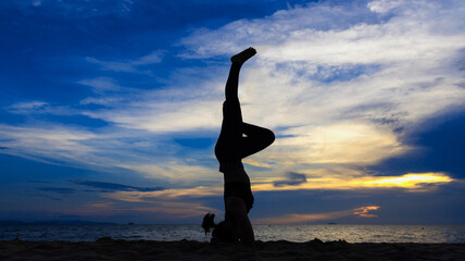 Silhouette image of a woman doing yoga on the beach at sunset. 
Young healthy woman, Asian girl practice Yoga on the beach Sunrise morning day Yoga on the beach healthy woman