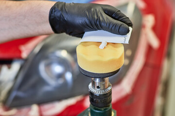 Gloved human hands placing a paste on a sponge from a polishing tool to polish car headlights...
