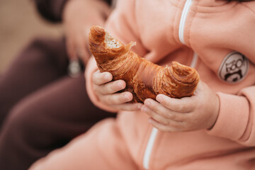Obraz na płótnie Canvas Close-up of a child's hand and a croissant. The child is eating a bun. Appetizing croissant in baby's hands.
