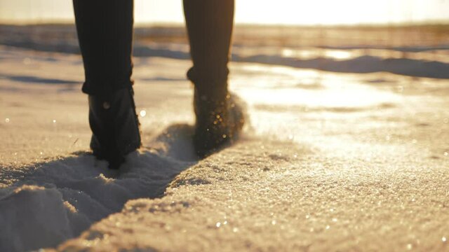 Female feet in black boots, winter walking in snow at sunset.