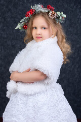 Obraz na płótnie Canvas Beautiful little girl in a white fur coat with a Christmas wreath on her head on a gray background. Christmas child.
