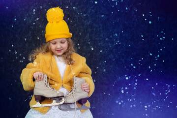 Obraz na płótnie Canvas Happy little girl in a yellow fur coat and a knitted hat with skates on a blue background sprinkled with snow.
