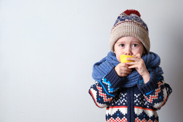 Sick child in clothes, toddler boy is standing on the grey background with a fever. llness child. Boy with lemon