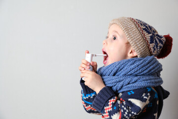 Sick child in clothes, toddler boy is standing on the grey background with a fever. llness child. Boy with medicine