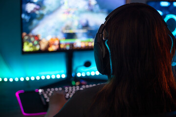 Close-up Back view of young female gamer playing video games and wearing headphone at home