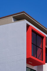 Low angle and side view of glass wall in red balcony frame on modern office building wall against blue sky background in vertical frame
