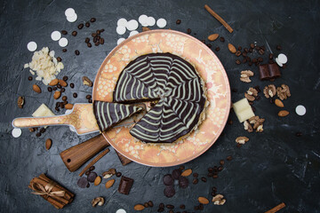 Chocolate sliced esterhazy cake with cream, frosting, nuts, cinnamon and almonds close-up view from the top on an orange-brown plate, on a wooden board on a dark concrete background