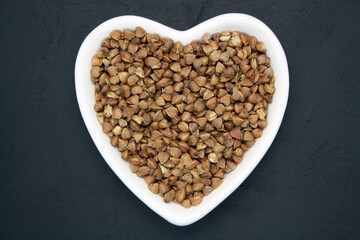 Buckwheat in a heart-shaped bowl on a black background.