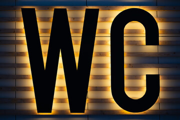 Yellow backlit black WC sign on wooden strips wall