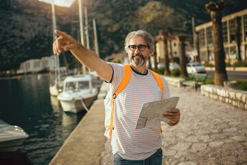 Smiling tourist mature man standing with map and backpack near the sea.