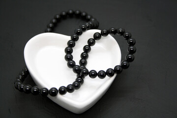 Black beads in a heart-shaped bowl on a black background.