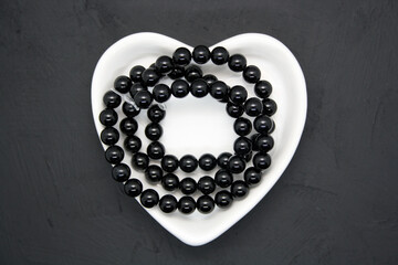 Black beads in a heart-shaped bowl on a black background.