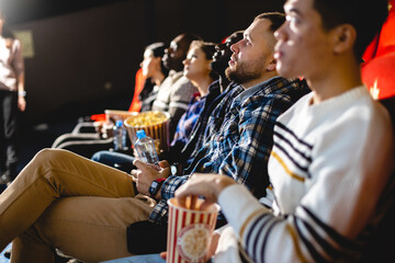 Friends watching a movie in the cinema with popcorn. People sit in the armchairs of the cinema and look at the screen