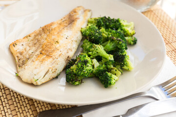 fried fillet of sea bass with garnish of broccoli on black warm stone plate