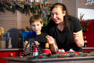 A little boy and mom are recording a stream or video on YouTube on a smartphone in the home kitchen.