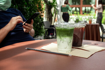 Green Matcha Latte and coffee with young man wearing protective face mask and using smart phone in a cafe.