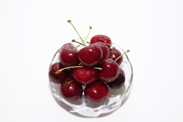 a pile of ripe red cherry berries lies on a transparent glass bowl background image on a white background close up