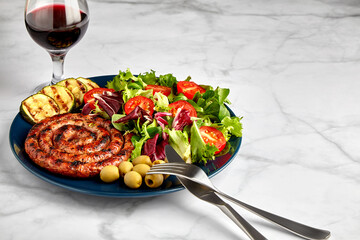 Spiral grilled sausage with vegetables and herbs on a plate with cutlery