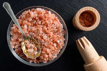 Fototapeta na wymiar Glass bowl of himalayan salt with small spoon and wooden salt mill on black background
