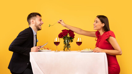 Loving Couple Feeding Each Other During Date On Yellow Background