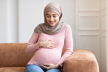 Pregnant Muslim Lady In Hijab Posing Sitting On Couch Indoor