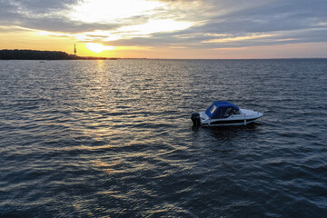 White pleasure boat against the setting sun on the Gulf of Finland on a summer day. Powerboat. Evening. Reflection of sun glare in the water.