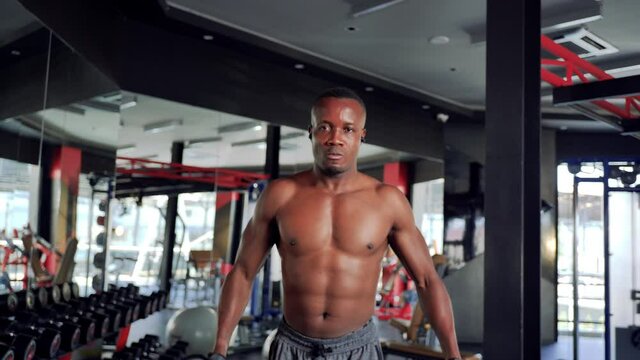 African male exercising with dumbbell at the gym Looking at camera, Muscular Build, fitness gym, healthy lifestyle. Slow motion