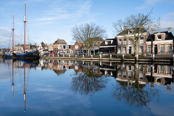 Fototapeta na wymiar Cityscape of Lemmer with the sailing yacht with two masts and houses mirrored in the water of the Dok in the Netherlands