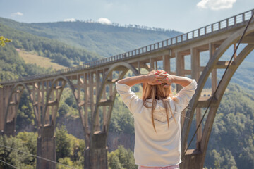 Girl with long hair stands against the background of beautiful arch bridge over Tara river, popular...