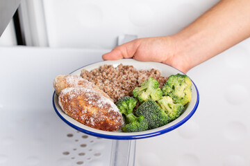 Frozen food. Hands are taking a plate of frozen cutlets and vegetables out of the freezer of the fridge.