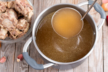 Saucepan with bouillon with a ladle on a wooden table. Bone broth