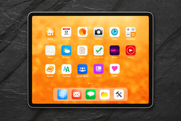 Digital tablet with bright home screen with application icons on dark background