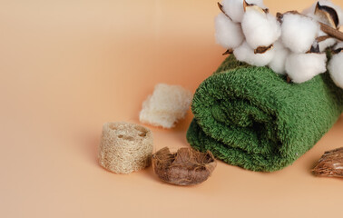 green, terry towel on a beige background, with a branch of cotton, close-up. Spa treatments