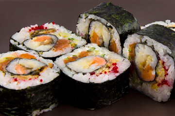 Complex roll - hot and cold with salmon, flying fish roe and avocado on white plate on black background