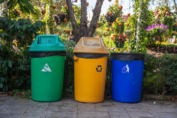 Three color trash cans (garbage bin) in the park beside the walk way.