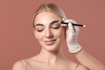 Young woman undergoing eyebrow correction procedure on color background