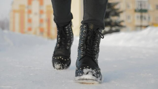 Female feet in black boots, winter walking in snow. Legs of woman walking in winter park.