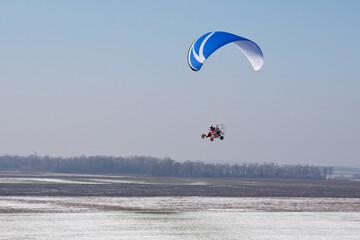 Aerial view of paramotor flying over the vastness of winter snowy French fields with horizon and blue sky