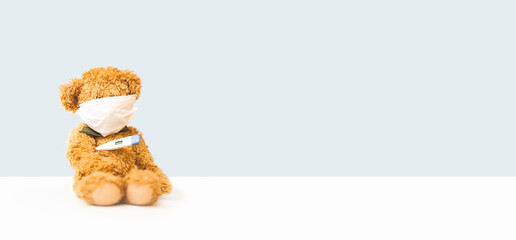 Toy bear sits in medical mask on light background with digital thermometer. Concept of health care....