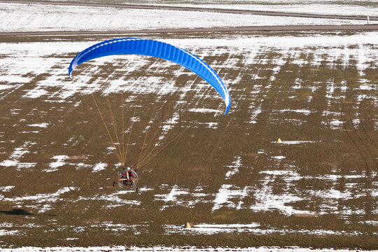 Motorized paraglider or paramotor preparing to land on a light aircraft runway for ULM in winter under the snow